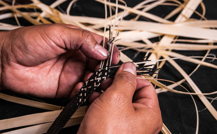 Foto de detalle de manos artesanas tejiendo la fibra de caña flecha
