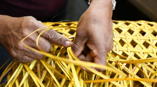 Fotografía de manos tejendo un cesto amarillo