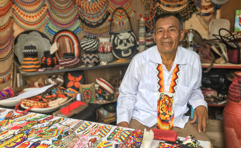 Fotografía del artesano José Flamedes Chirimía en un stand de feria junto a artesanías elaboradas por su grupo Tai K'a. 