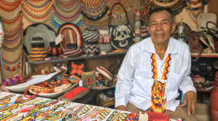 Fotografía del artesano José Flamedes Chirimía en un stand de feria junto a artesanías elaboradas por su grupo Tai K'a. 
