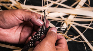 Foto de detalle de manos artesanas tejiendo la fibra de caña flecha