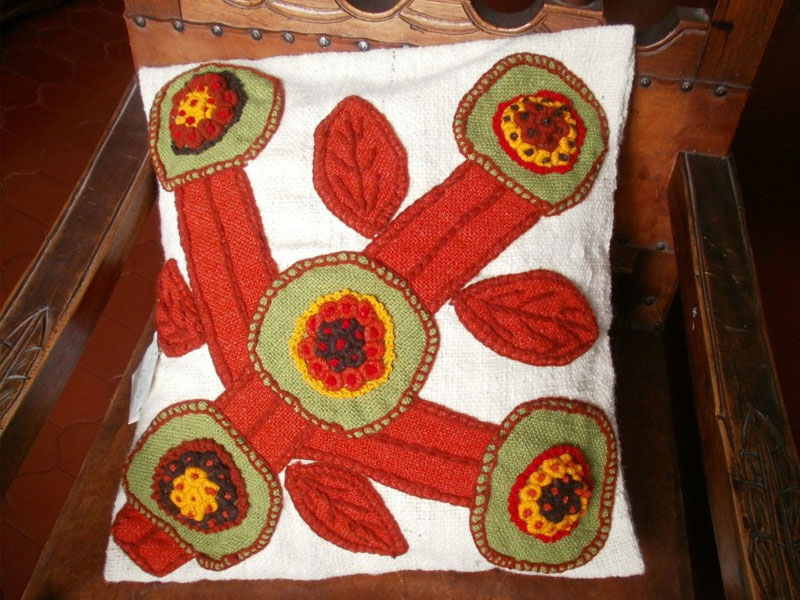 Cojín bordado en lana virgen, con aplicaciones de paño sobre paño. Medidas: 0.45 m x 0.45 m